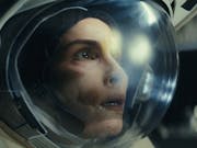 Close up of a white woman in space in an astronaut's clothing and helmet looking shocked