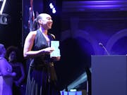A Black woman in an elegant black dress on stage accepting a blue BIFA award