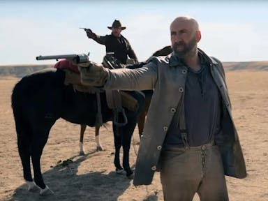 A white man in old west clothing pointing an old style pistol, as another white man wearing a cowboy hat, riding a horse, also points a gun in the same direction 