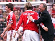 Two male footballers in red and white kit, one with 'Beckham 7' on back of shirt, and a football manager on the football field celebrating