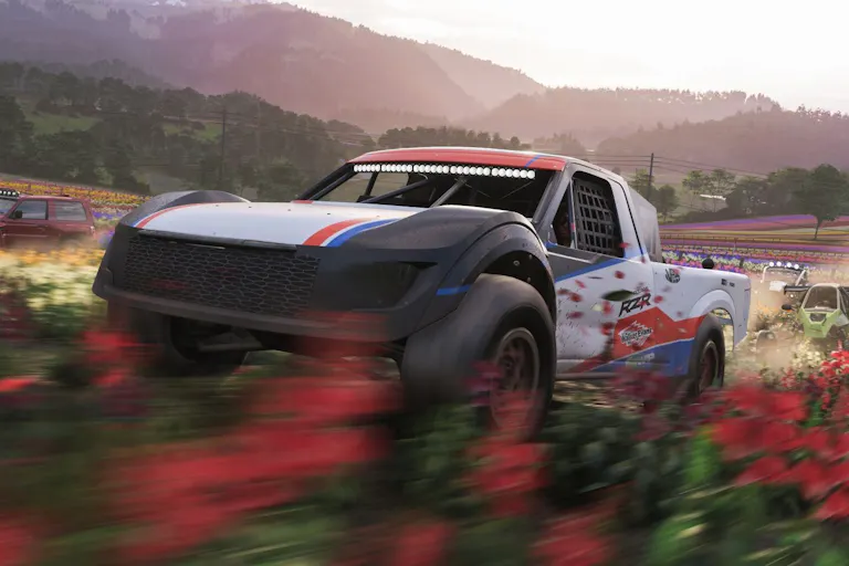A white red and blue car driving fast through a field of red flowers