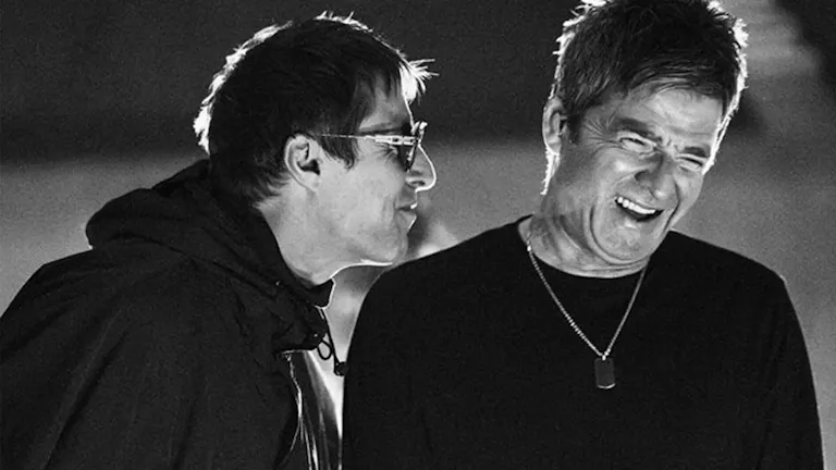 A black-and-white close-up still of two older men (Liam and Noel Gallagher of the band Oasis) mid-laugh