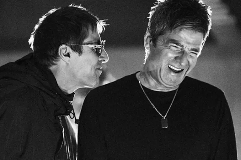 A black-and-white close-up still of two older men (Liam and Noel Gallagher of the band Oasis) mid-laugh