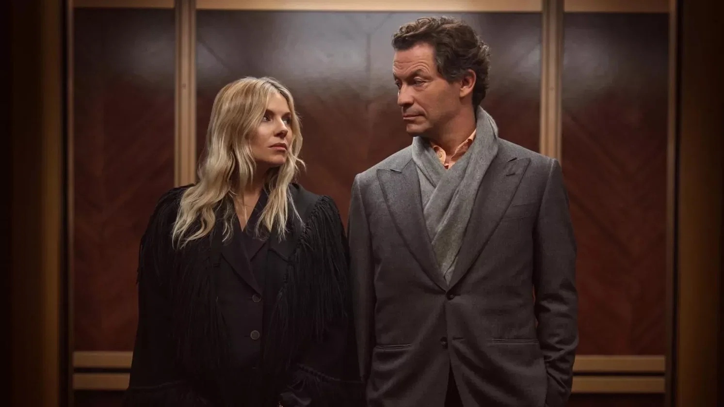 A man and a woman in an elevator looking at eachother with stern looks on their faces