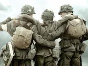 Three army soldiers in their gear. The two on either end holding the middle guy up