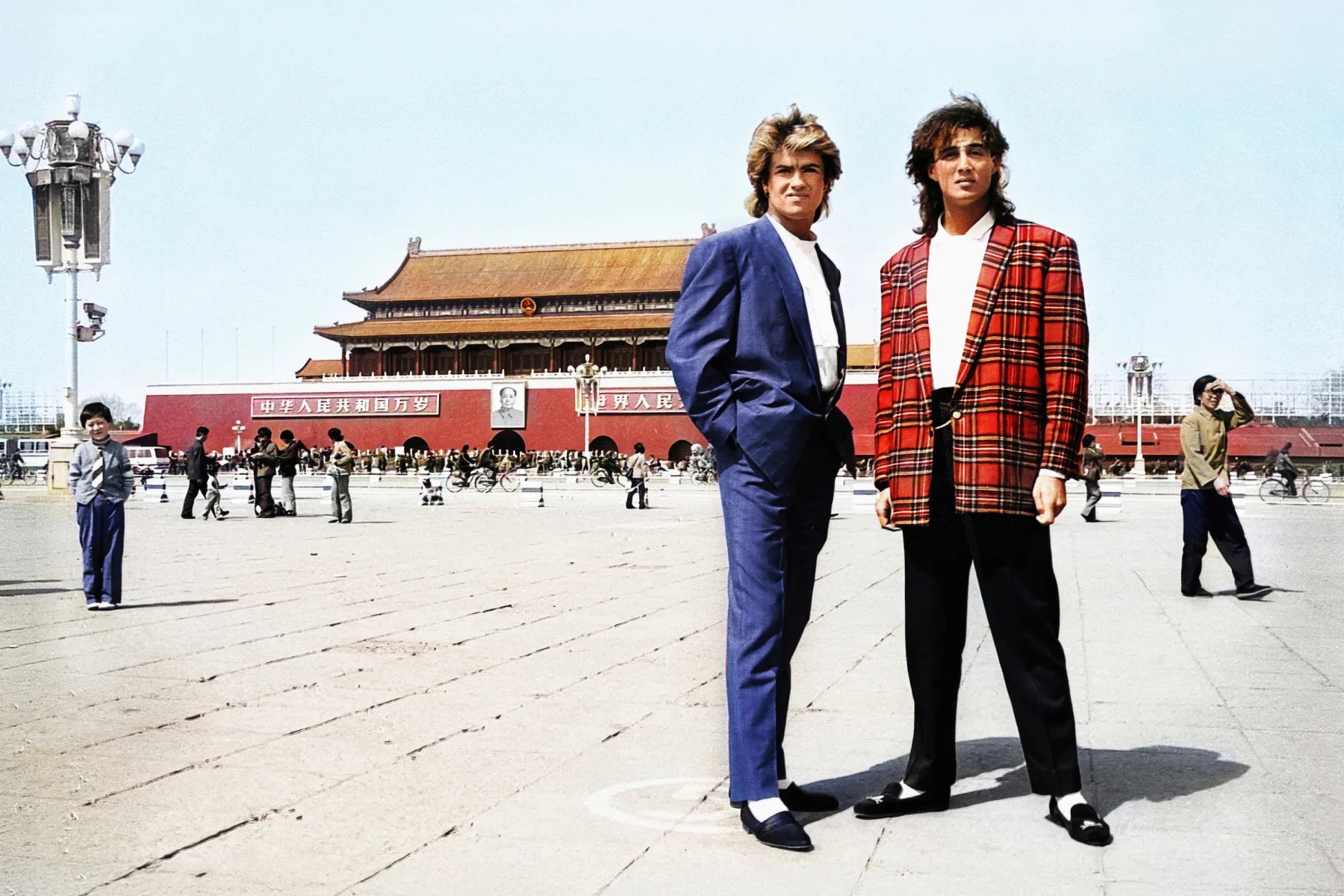 Two young white men in bright red and blue suits, standing in a Chinese town