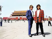 Two young white men in bright red and blue suits, standing in a Chinese town