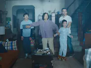 A mum, dad, and two children in their basement, illuminated by a blue light, all with a scared look on their face