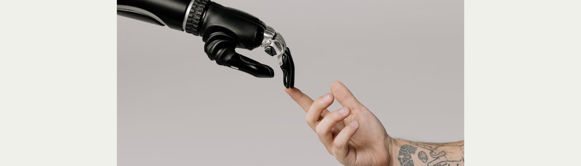 A robot arm and human arm extend towards each other. In the middle of the photo the two index fingers touch each other.