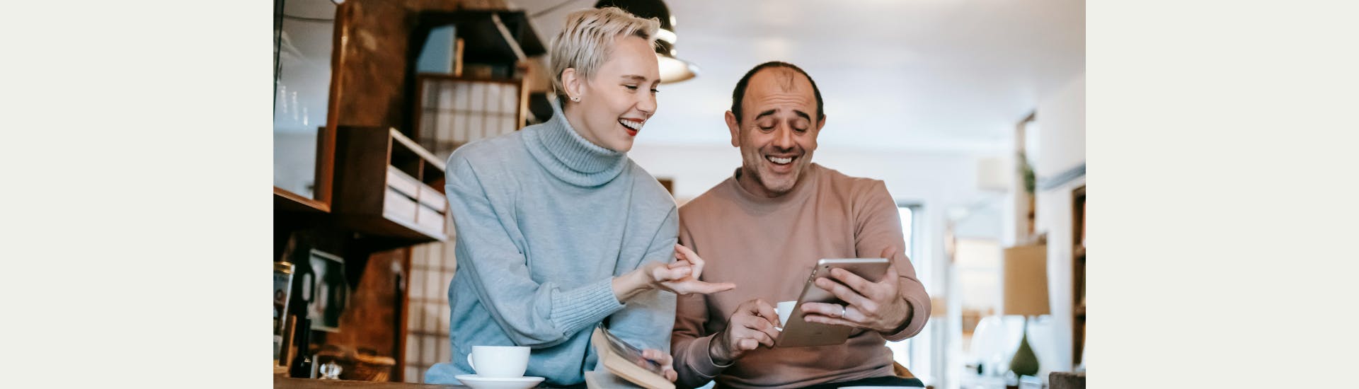 Een man en vrouw zitten in een cafe. Ze kijken lachend naar een tablet.