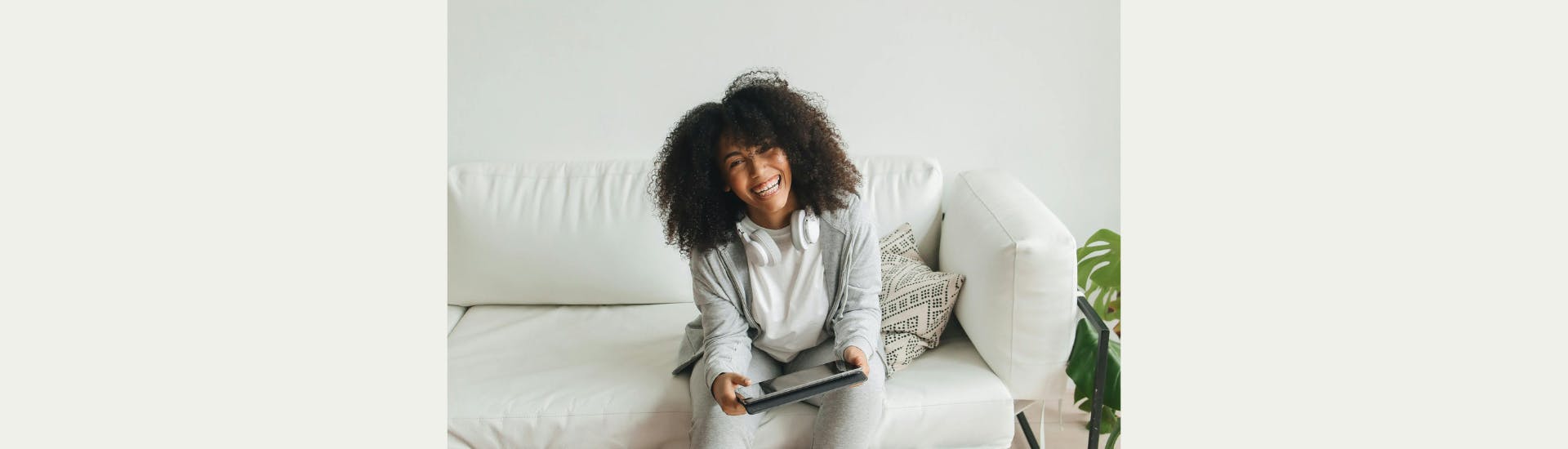 Een vrouw met tablet in de hand en koptelefoon om de nek lacht breed naar de camera.