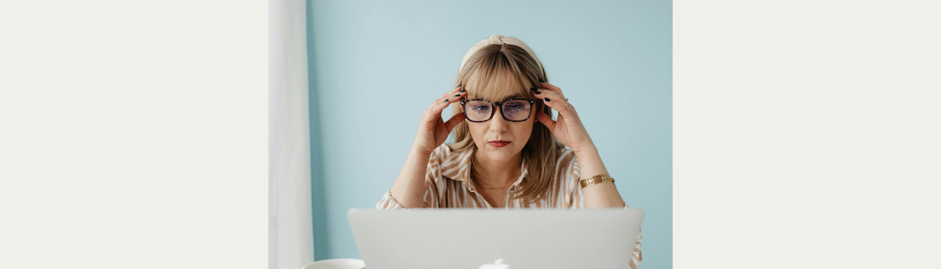 Een vrouw met bril op kijkt bedenkelijk naar een laptop. 