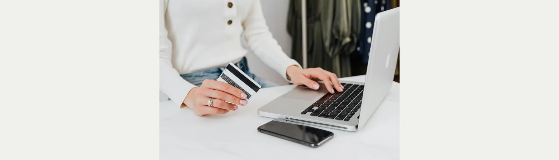 A woman with a credit card in her hand stands by an open laptop.