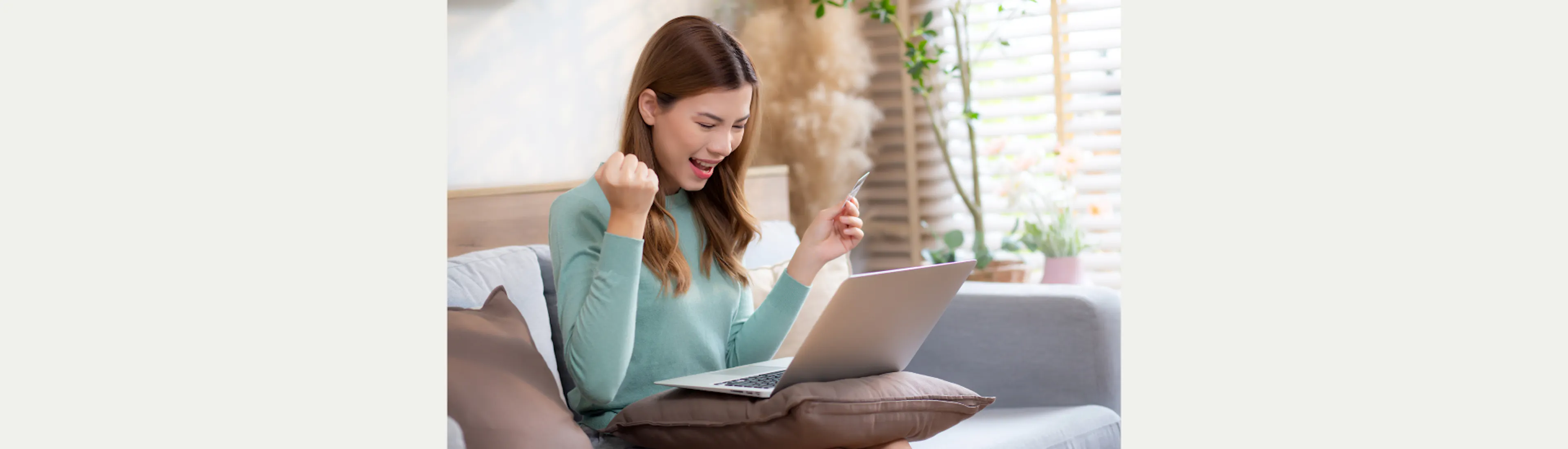 Een vrouw met opengeklapte laptop op schoot en creditcard in de hand juicht. 