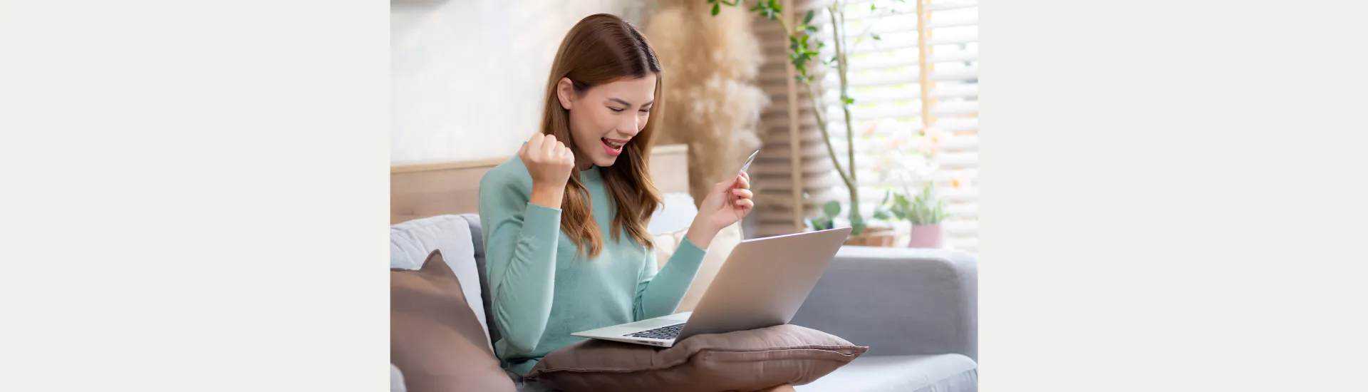 Een vrouw met opengeklapte laptop op schoot en creditcard in de hand juicht.