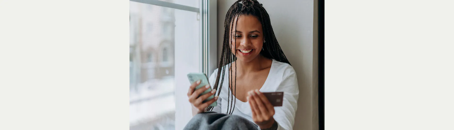 Een vrouw met creditcard in de hand kijkt lachend naar een telefoon.