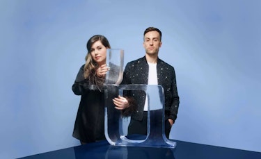 Nadège Dionne-Tremblay and Karim Marier-El Khayat, cofounders of Sculpture, standing in front of a blue background. Both are dressed in fancy black clothing. Nadège is holding an ice sculpture of a letter in the Sculpture font. Karim is standing beside her, hands in his pockets.
