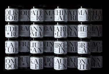 An image of multiple Sculpture branded candles stacked on top of each other, on a black background. Each candle is personalized with people's names.