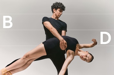 A duo of dancers photographed in a studio against a neutral background, showing a male dancer lifting a female dancer in a suspended choreographic position. The letters “B” and “D” appear on either side of the composition, overlaid on a graphic grid that structures the image and emphasizes balance and axis.