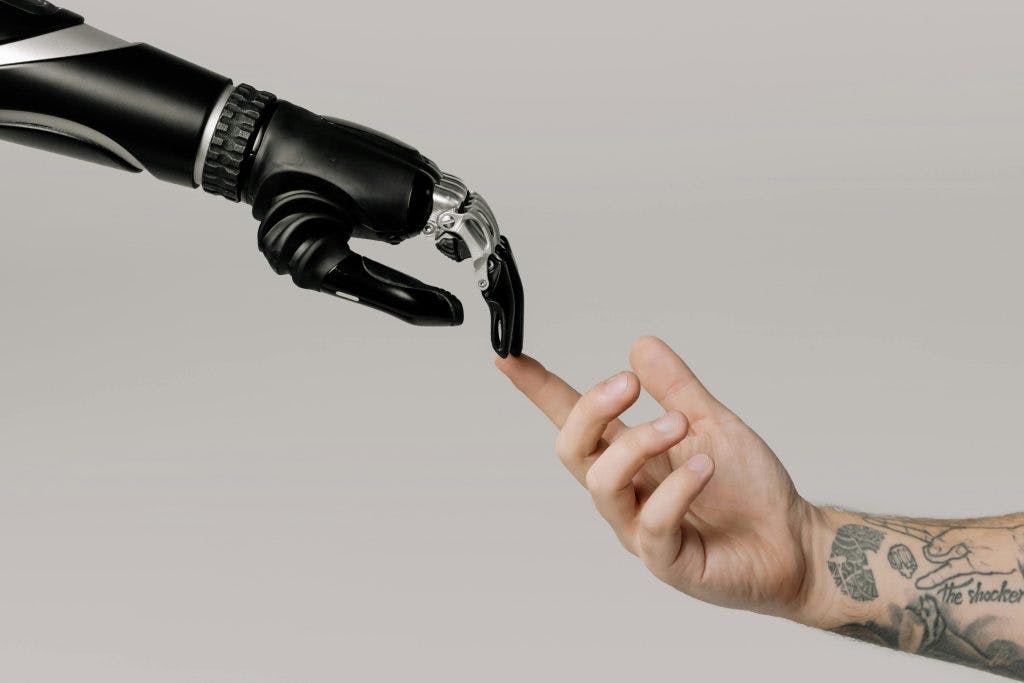 A Mechanical Hand Reaches Out To Touch A Human Hand.