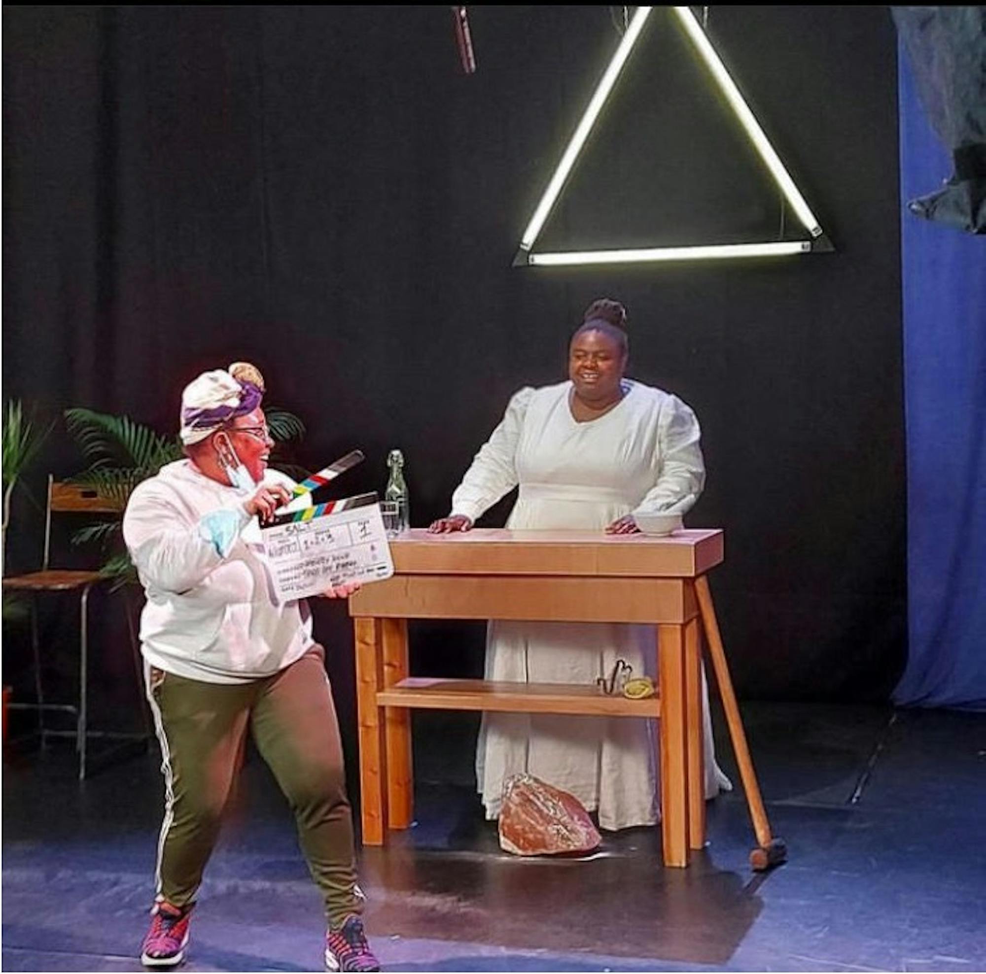 Selina and Toni-Dee, both young Black women, on a stage set. Toni holds a film clapper board.