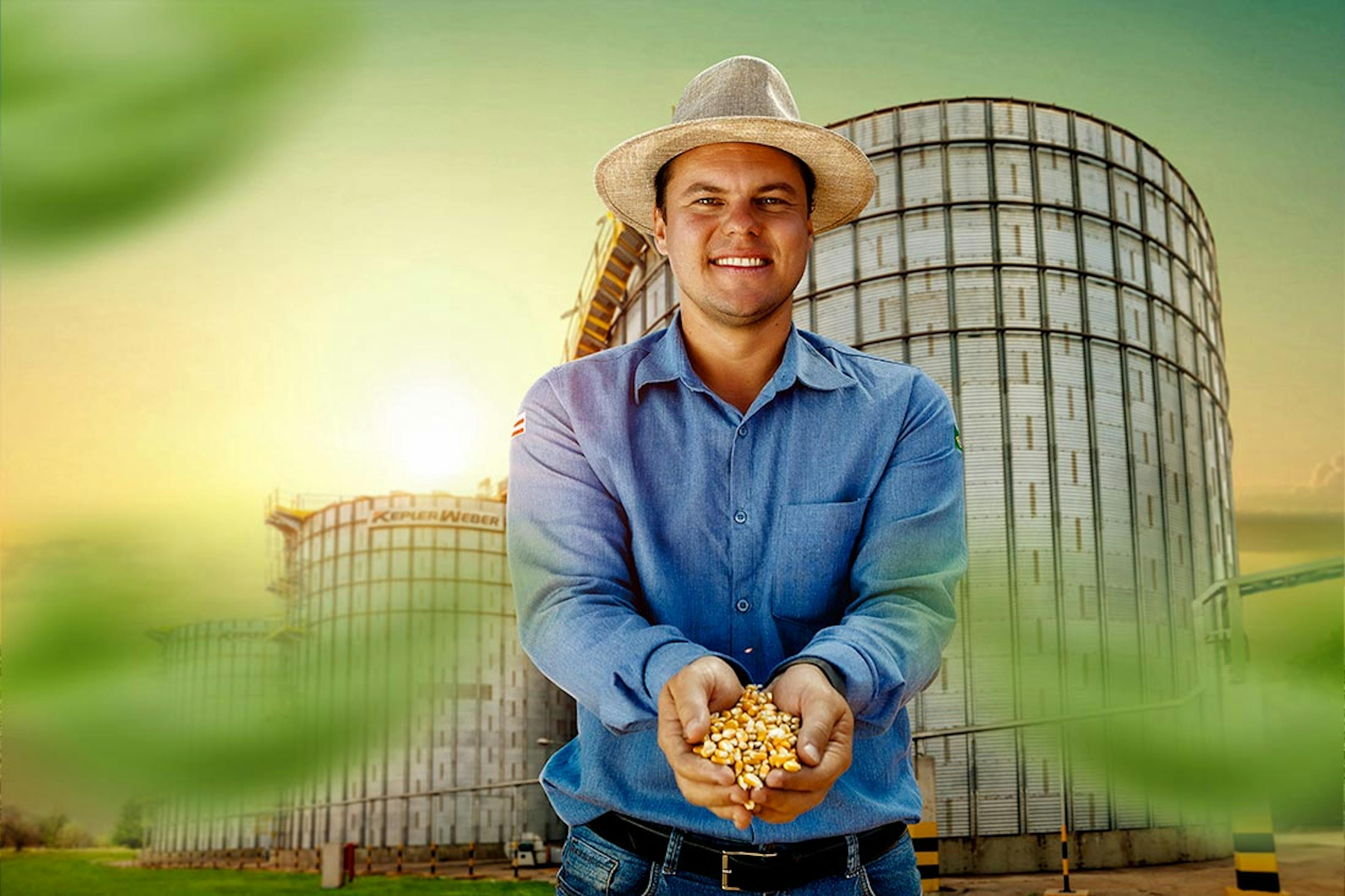 Homem segurando grãos de milho em frente a um silo em ambiente rural.