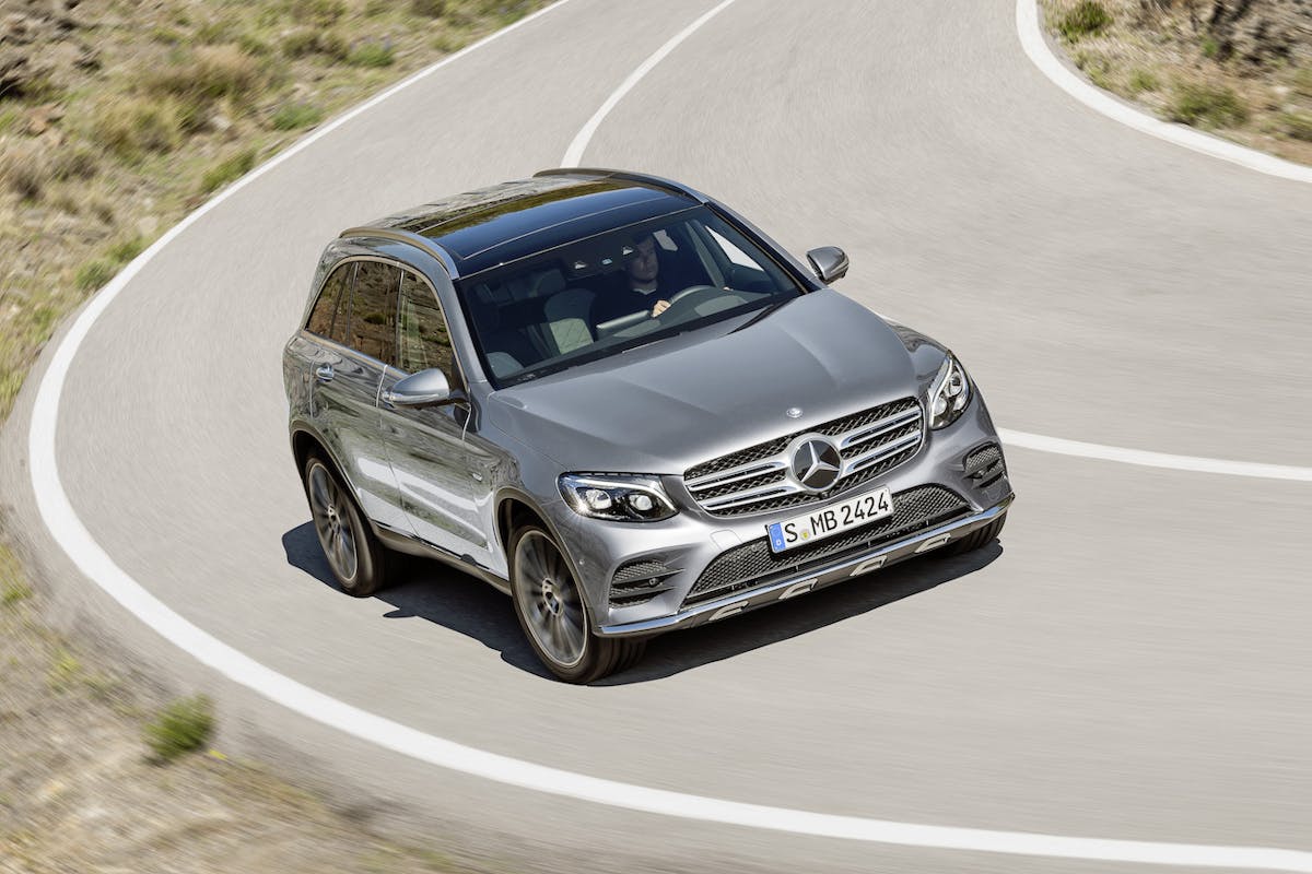 Silberner Mercedes-Benz SUV fährt auf kurviger Bergstraße bei sonnigem Wetter, umgeben von kahlem, grasbewachsenem Gelände.