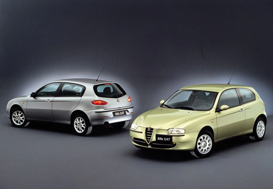 Zwei Alfa Romeo 147 Autos: ein silbernes und ein olivgrünes Modell, nebeneinander auf dunklem Hintergrund.