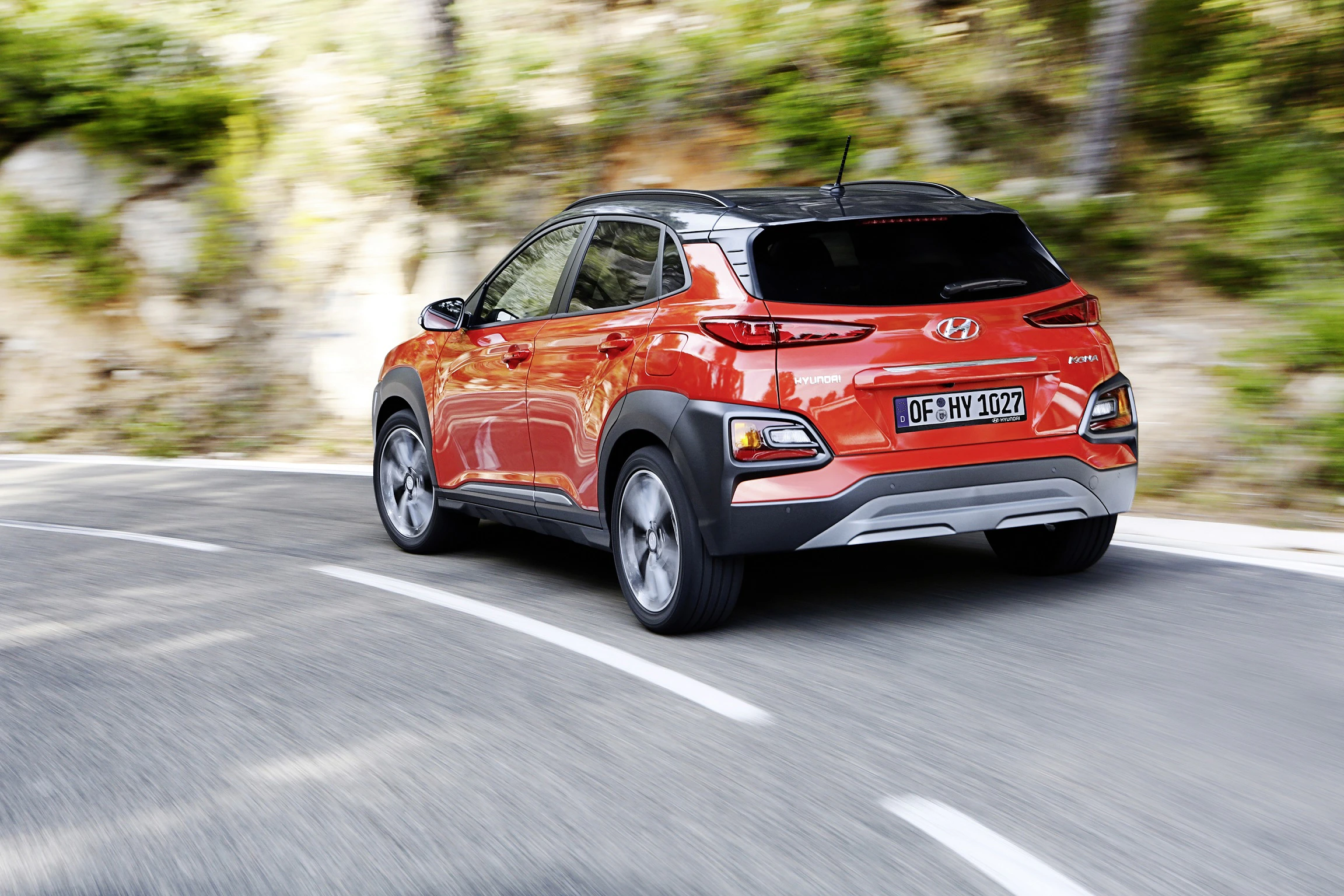 Roter Hyundai SUV fährt auf kurviger Straße in bewaldeter Gegend. Autokennzeichen ist sichtbar.
