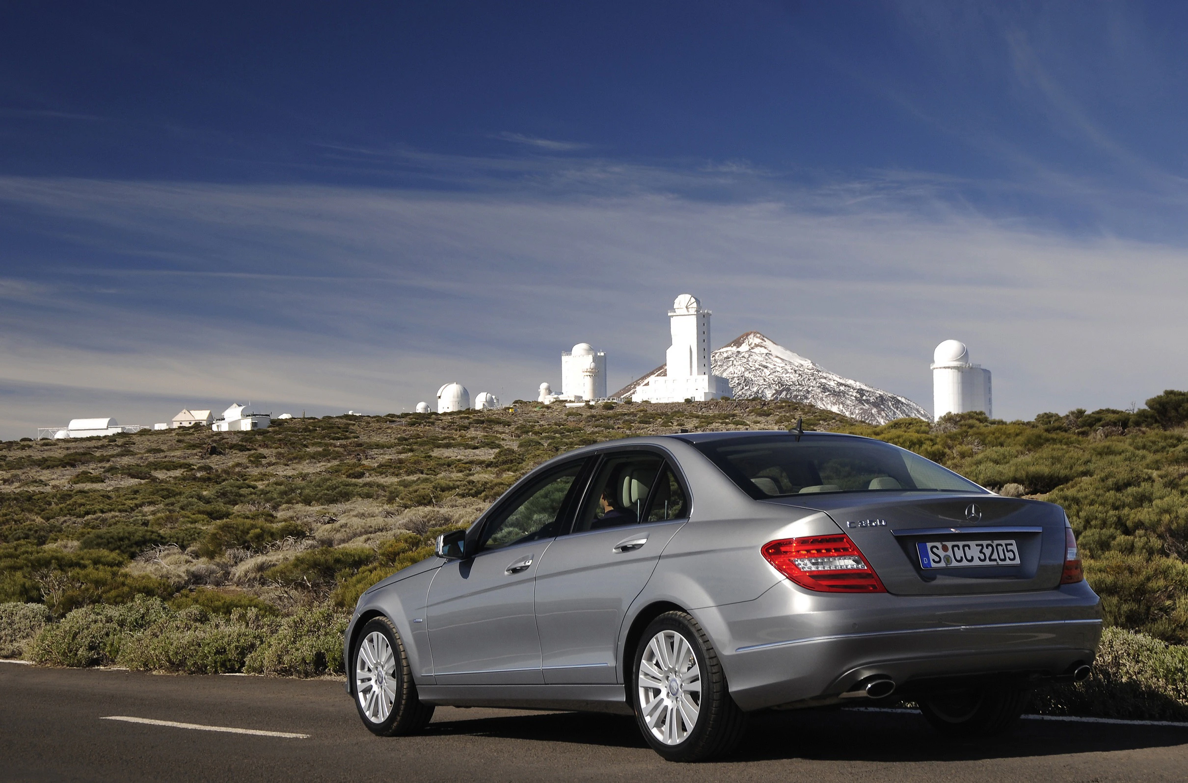 Silberner Mercedes vor einer Observatoriumslandschaft mit blauem Himmel und Bergen im Hintergrund.