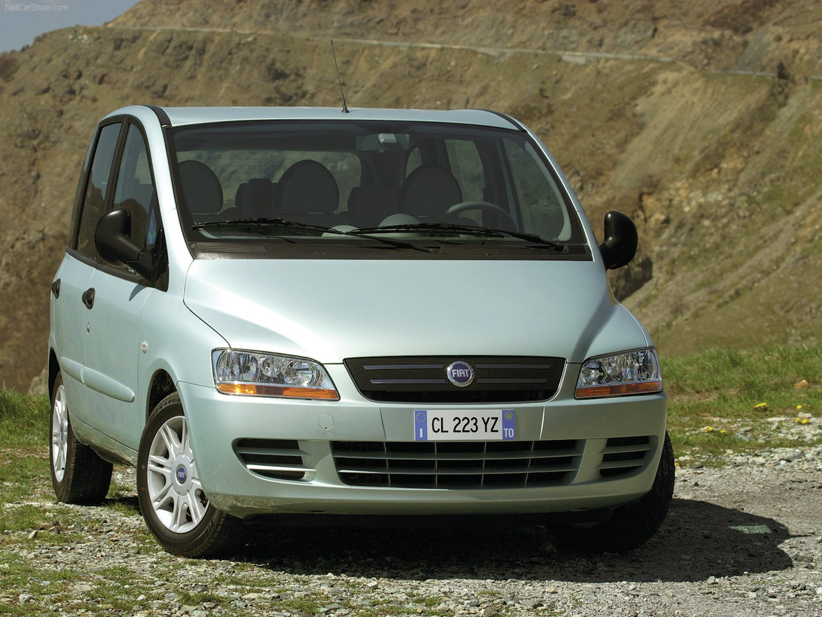 Ein heller Fiat Multipla steht vor einer felsigen Berglandschaft auf einem unbefestigten Weg.