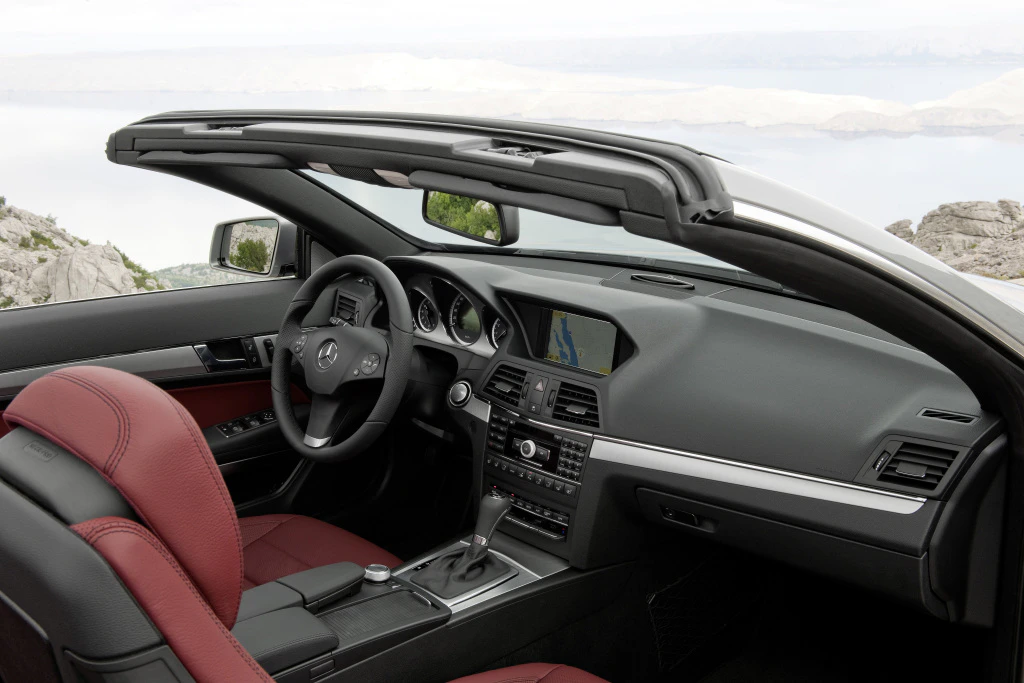 Innenraum eines schwarzen Cabriolets mit roten Ledersitzen und geöffnetem Verdeck. Modernes Armaturenbrett mit Multimedia-Anzeige.