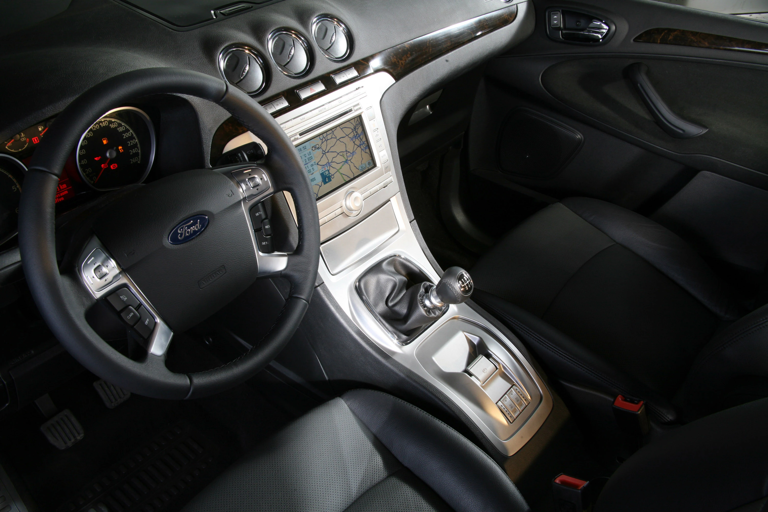 Innenraum eines Autos mit manuellem Schaltgetriebe, Lenkrad, Tachometer und eingebautem Navigationsbildschirm. Dunkles Interieur.