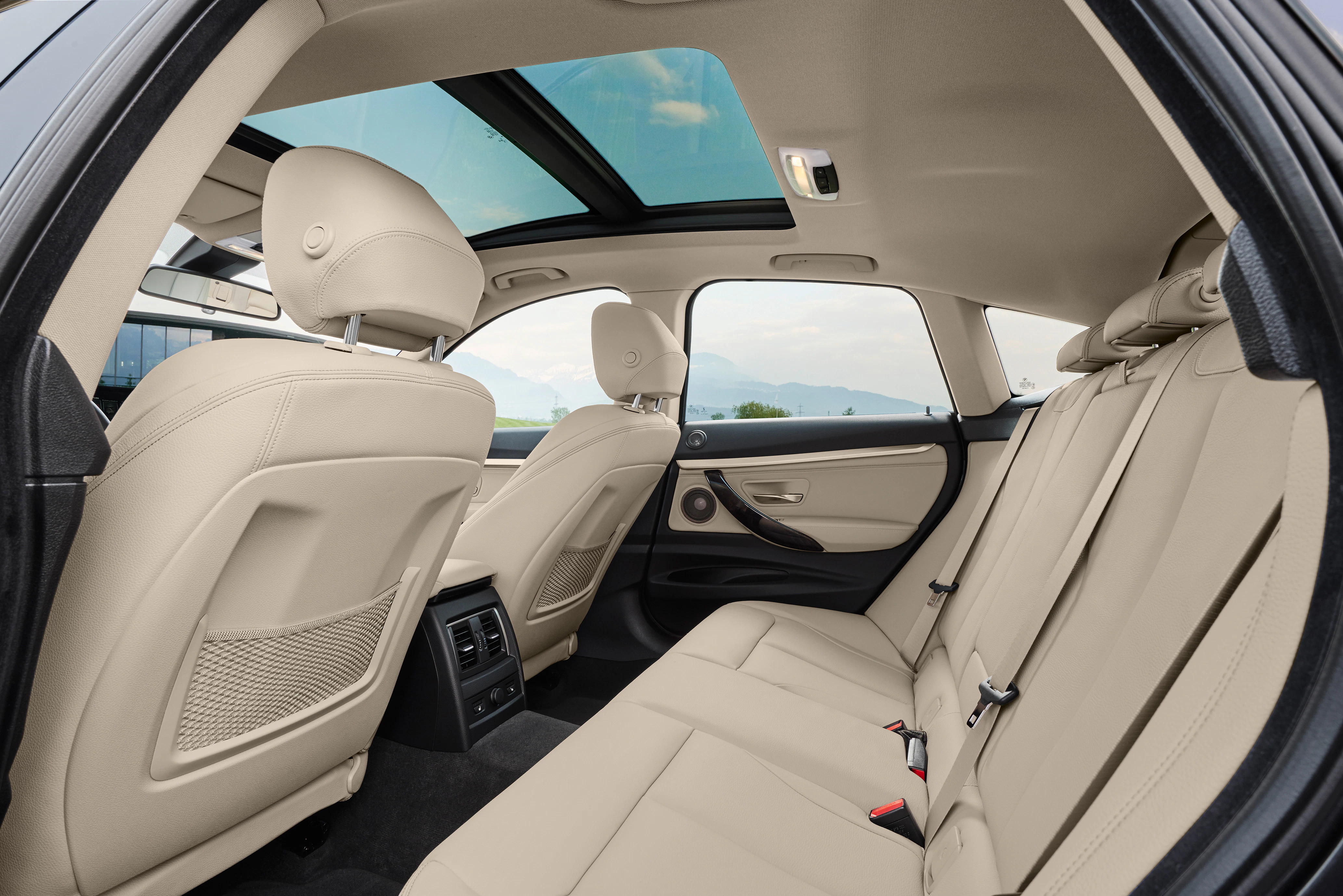 Rückbank eines Autos mit beigen Ledersitzen, Panoramadach und Blick auf die Vordersitze. Helle und geräumige Innenausstattung.