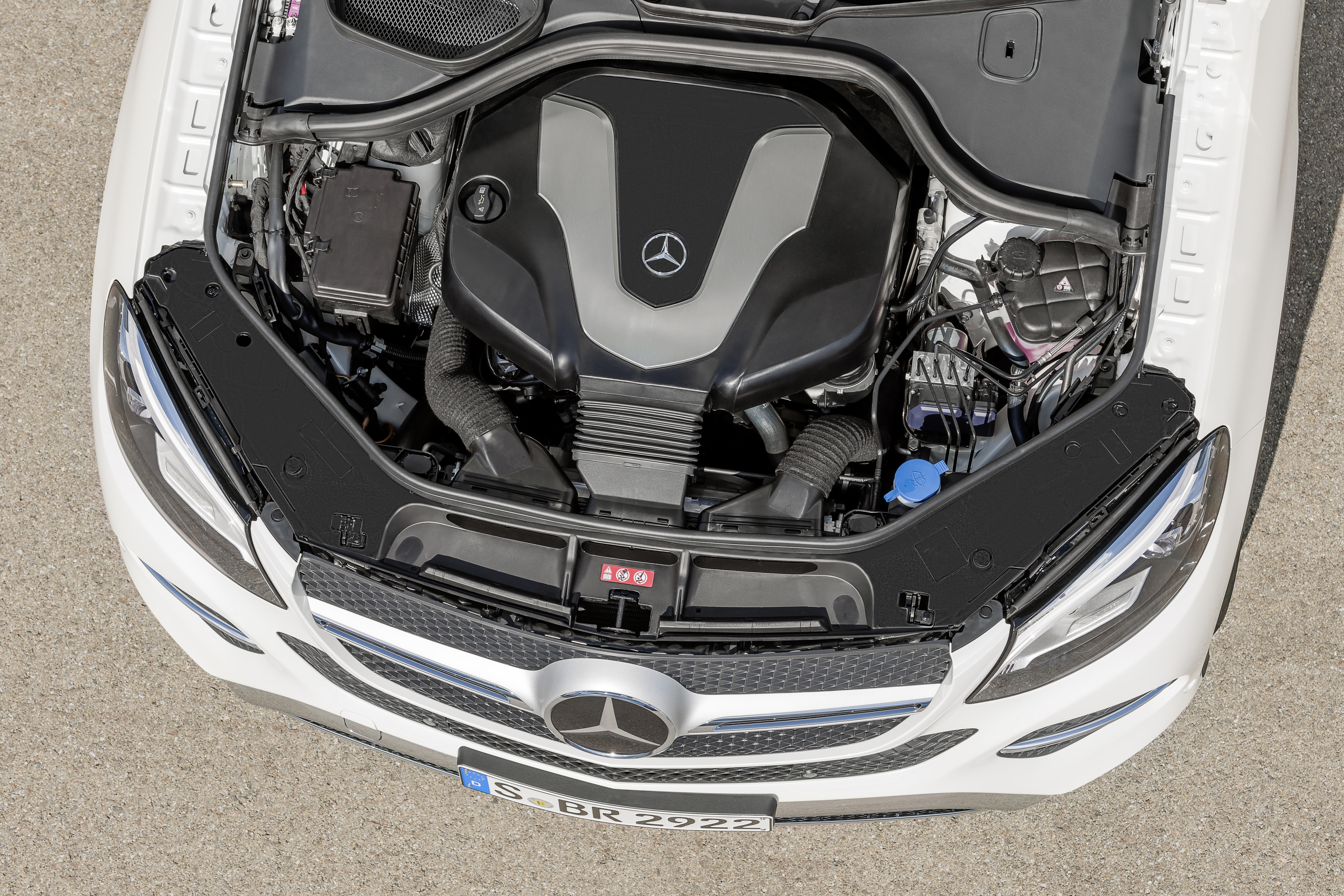 Motorraum eines Mercedes-Benz mit sichtbarem Markenlogo, geöffnet. Gut sichtbare Motorabdeckung und technische Details. Fahrzeug frontal aufgenommen.