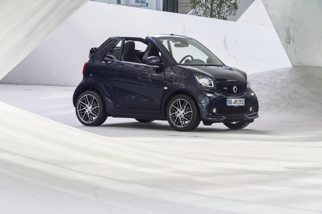 Schwarzes Smart-Cabrio in einem weißen, modernen Raum geparkt. Das Auto hat ein offenes Verdeck und sportliche Felgen.