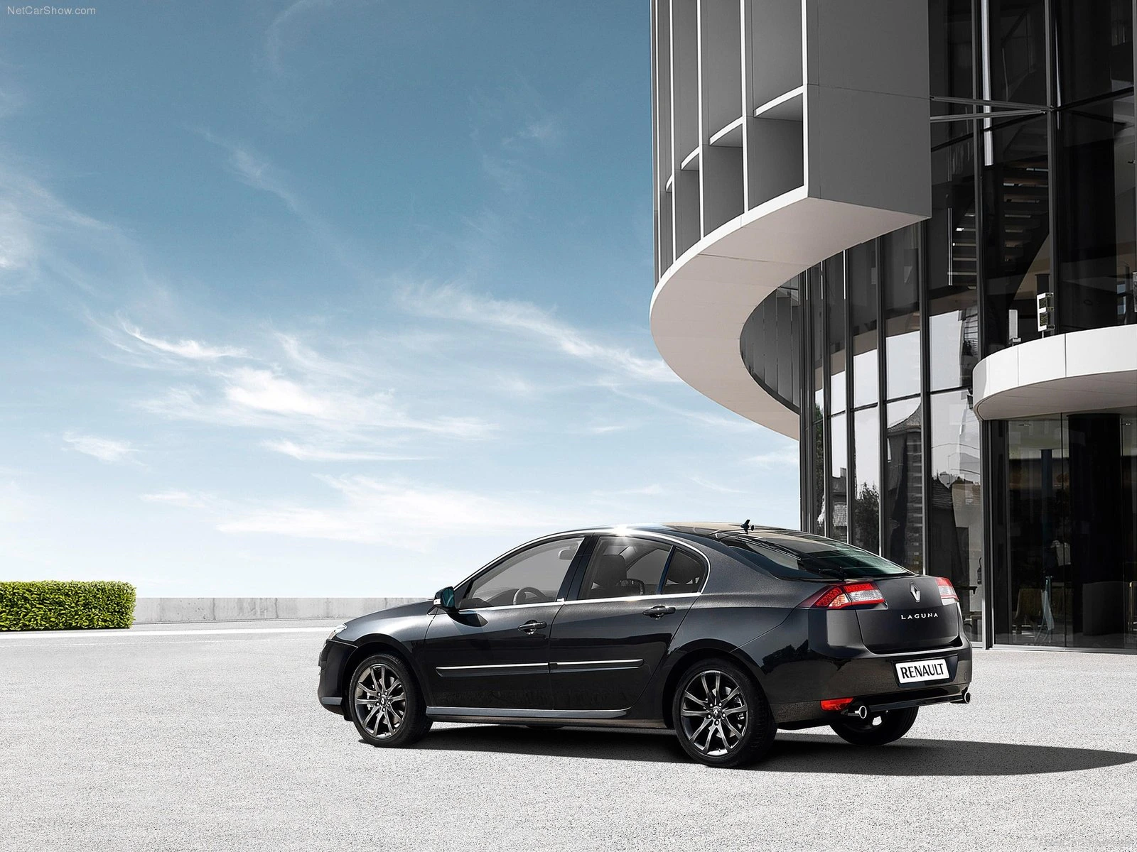 Schwarzer Renault Sedan steht auf einem Parkplatz neben einem modernen Gebäude unter blauem Himmel.