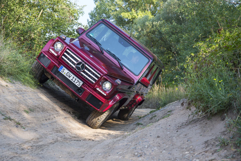 Roter Geländewagen auf unebenem Offroad-Pfad im Wald, leicht zur Seite geneigt.