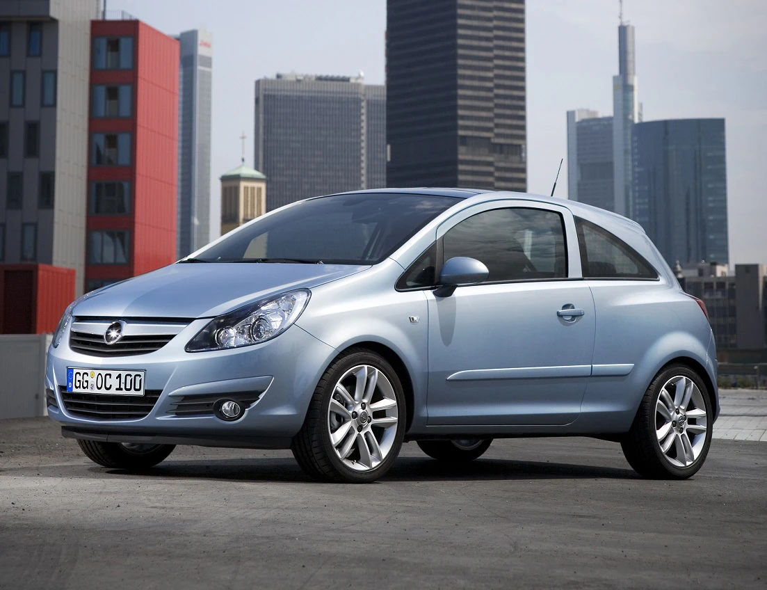 Silberner Opel Corsa steht auf einem Parkplatz vor einer urbanen Skyline mit modernen Hochhäusern im Hintergrund.