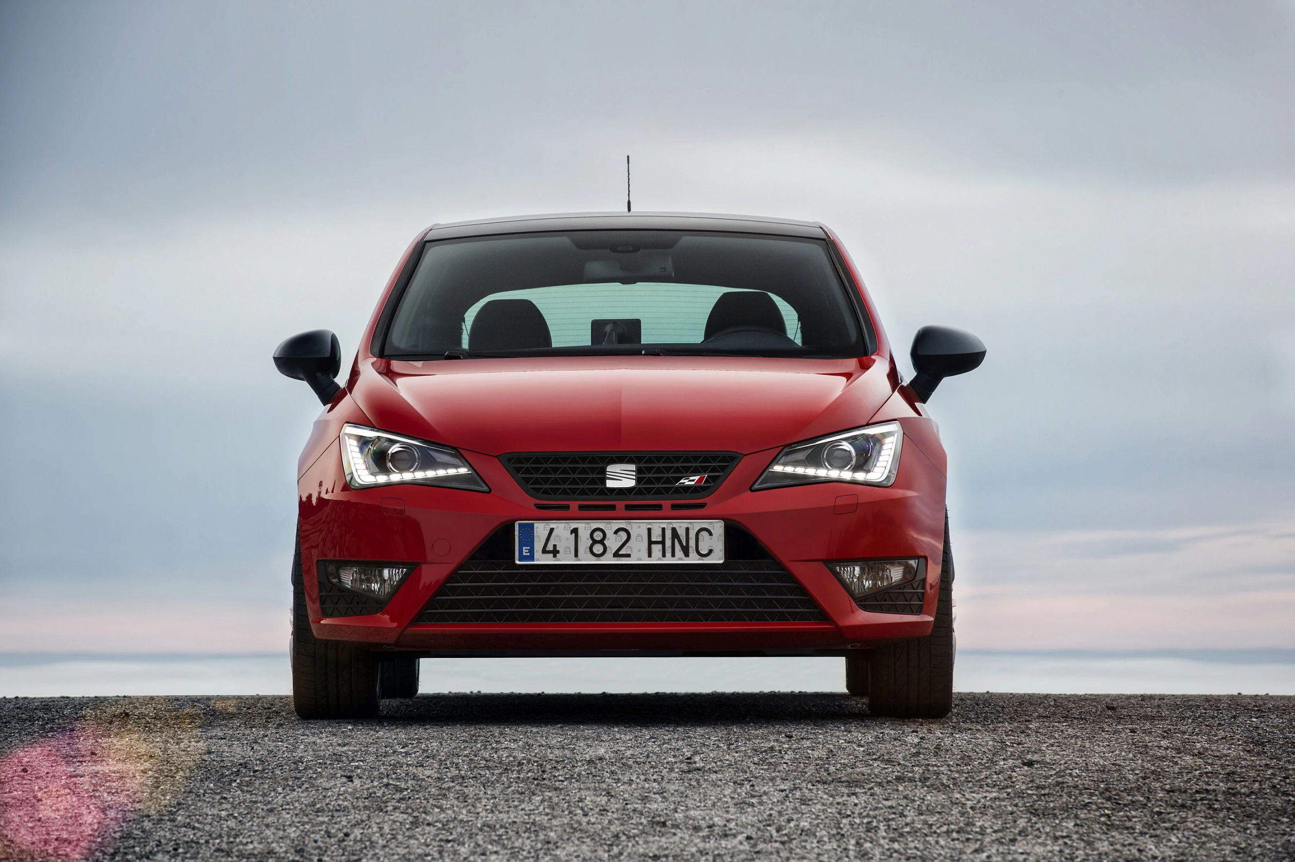 Roter Seat Ibiza steht frontal auf einer Kiesfläche, grauer Himmel im Hintergrund. Nummernschild zeigt "4182 HNC".