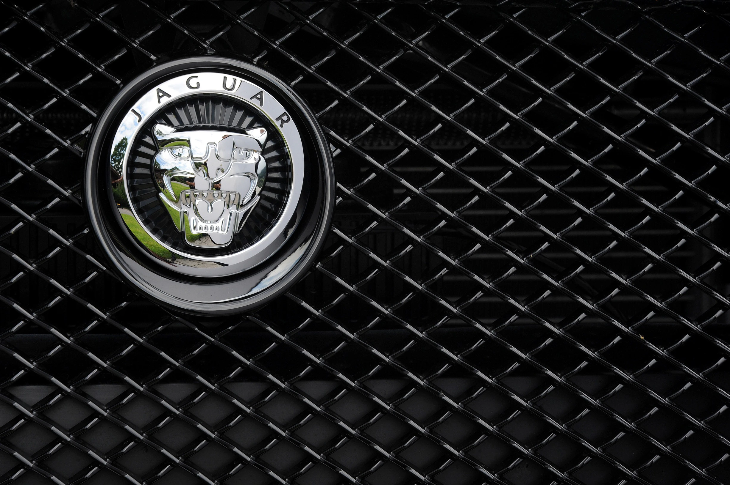 Nahaufnahme des Jaguar-Logos auf einem glänzenden schwarzen Kühlergrill mit Gittermuster.
