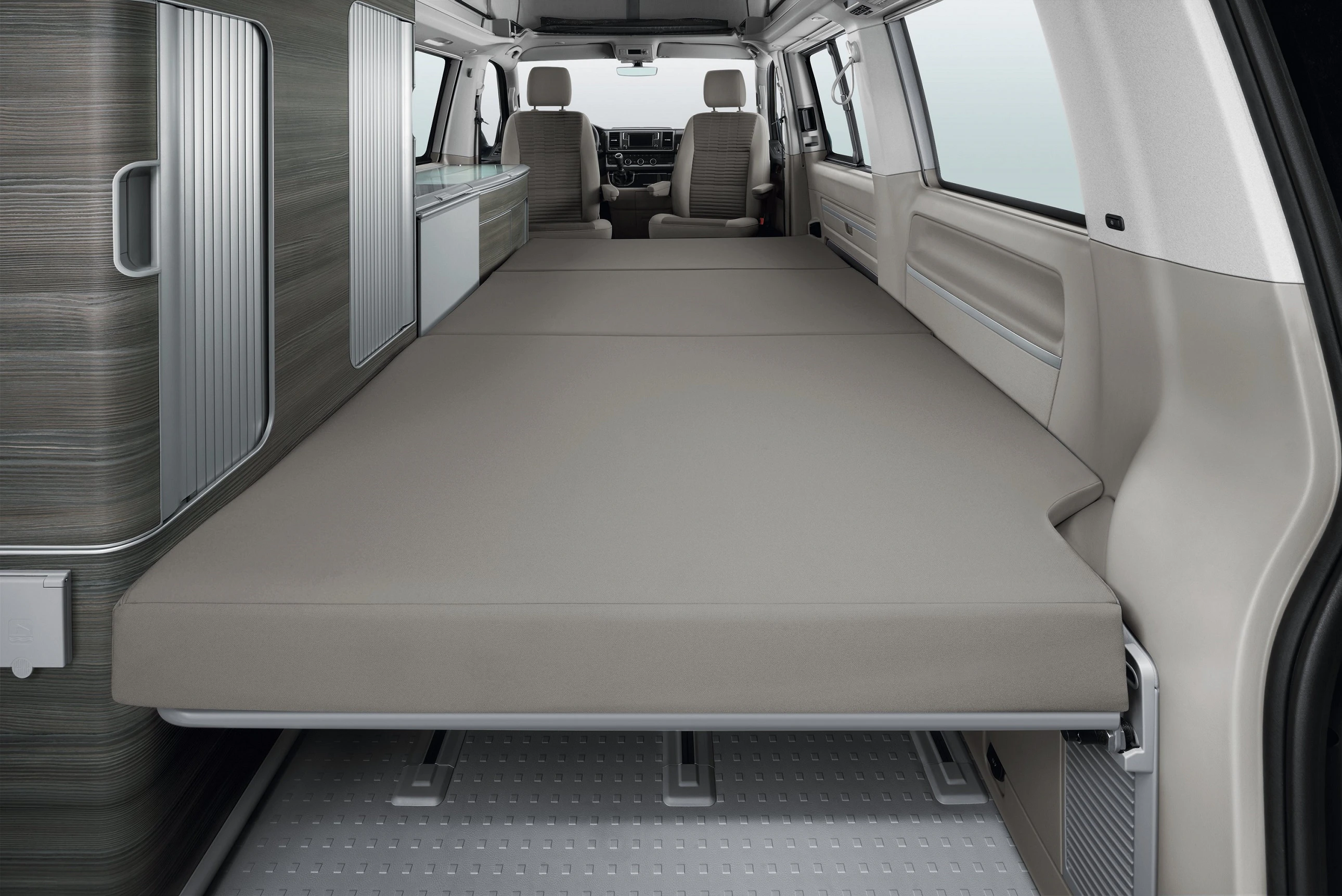 Innenraum eines Wohnmobils mit ausgeklapptem Schlafbereich, grauen Matratzen und zwei vorderen Sitzen in einem modernen Design.