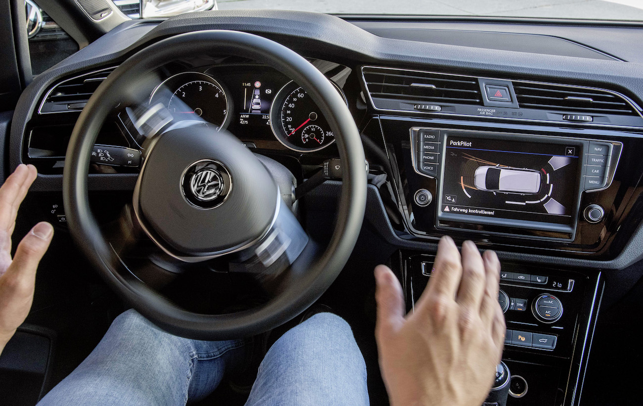Ein Autofahrer lässt das Lenkrad los, während ein Parkassistenz-System im Auto aktiviert ist. Anzeigen auf dem Bordcomputer.