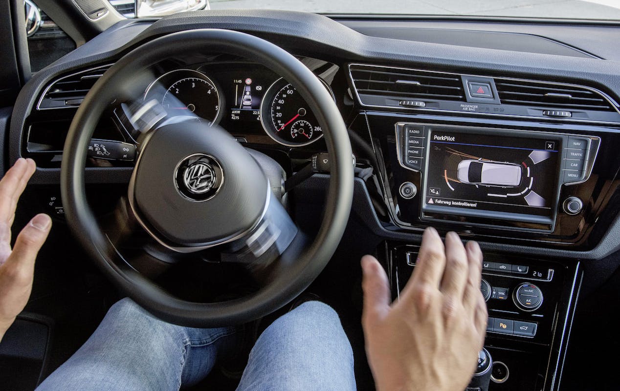 Ein Autofahrer lässt das Lenkrad los, während ein Parkassistenz-System im Auto aktiviert ist. Anzeigen auf dem Bordcomputer.