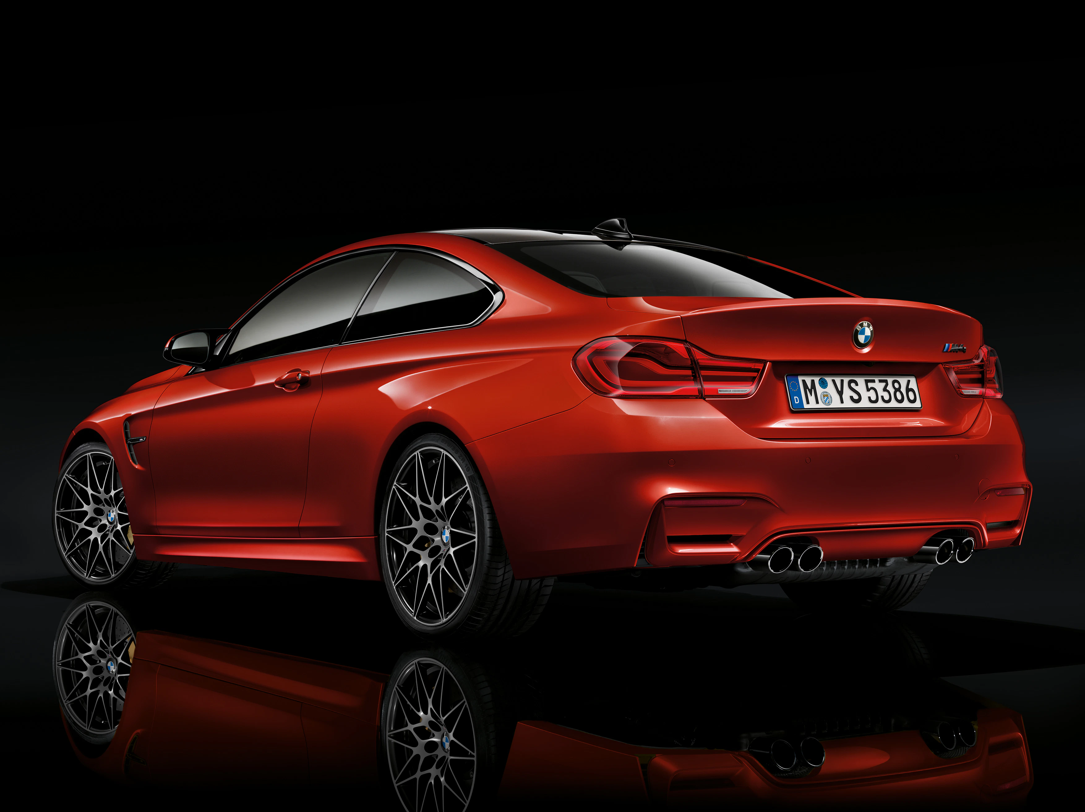 Rotes Sportcoupé mit getönten Fenstern und glänzenden Felgen, von der Seite und leicht von hinten, auf schwarzem Hintergrund dargestellt.
