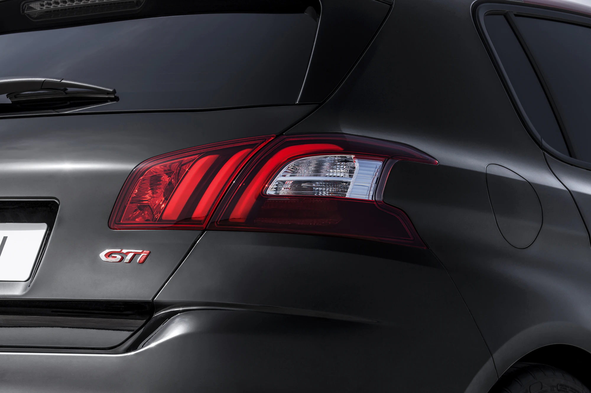 Nahaufnahme eines dunklen Autos mit dem "GTI"-Logo am Heck und roten Rücklichtern.