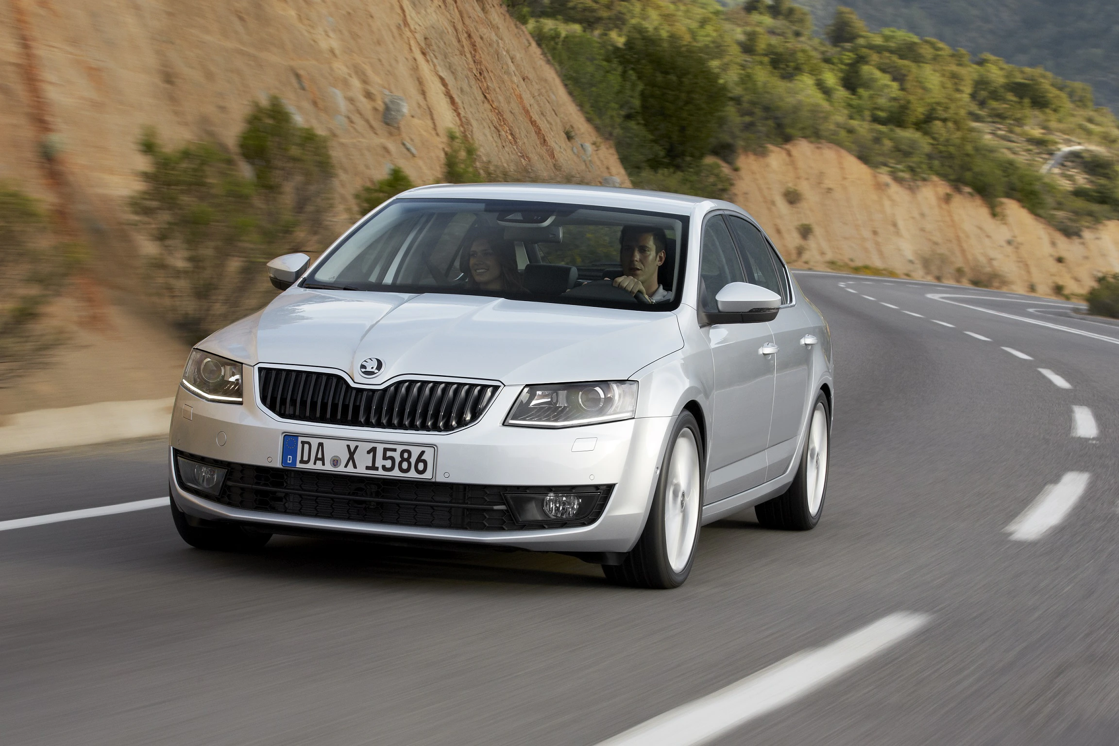 Silberner Skoda Octavia fährt auf einer kurvigen Straße durch eine bergige Landschaft.