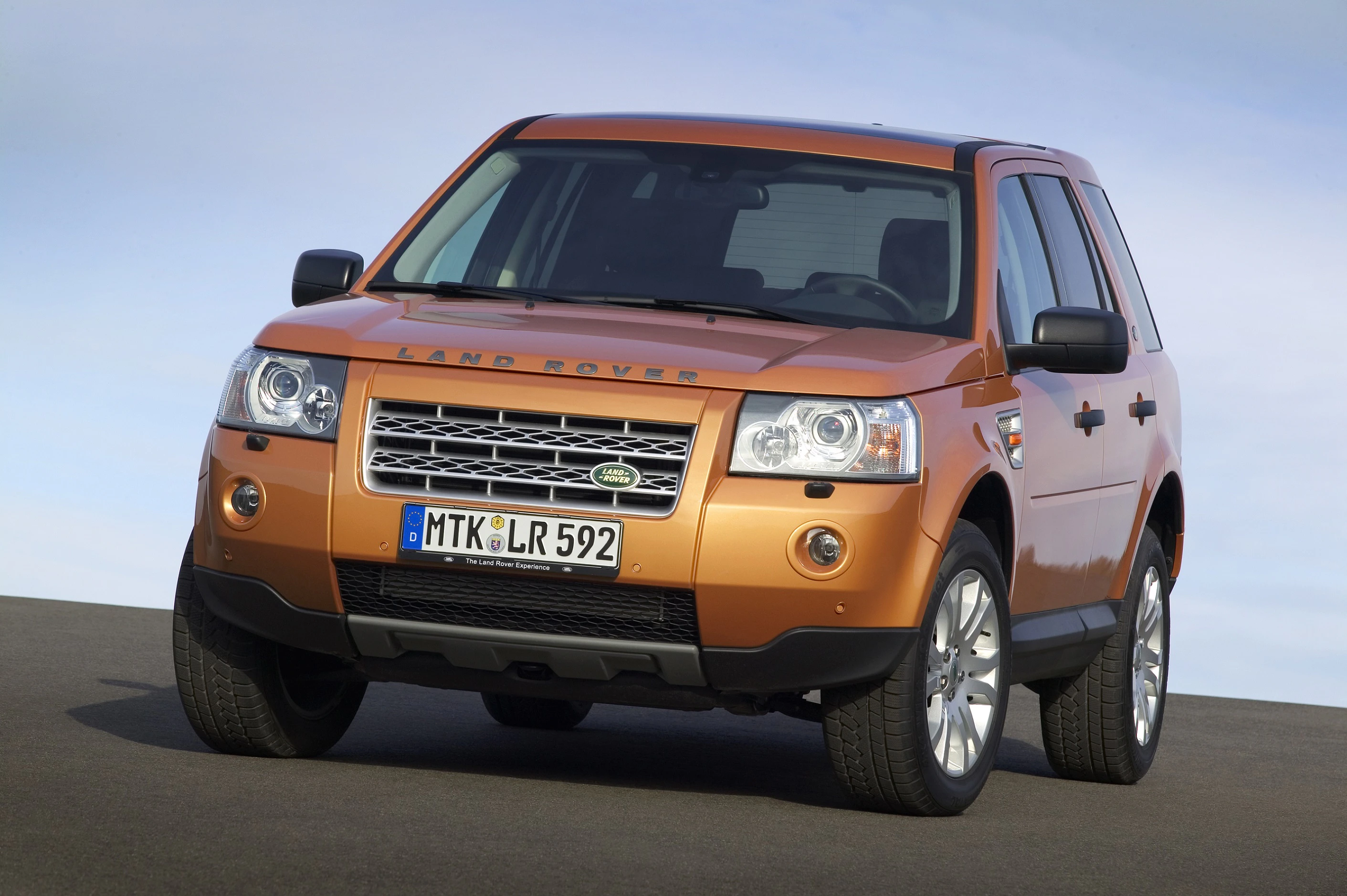 Orangefarbener Land Rover Freelander steht auf einer Straße vor blauem Himmel. Das Fahrzeug zeigt eine deutsche Nummerntafel.