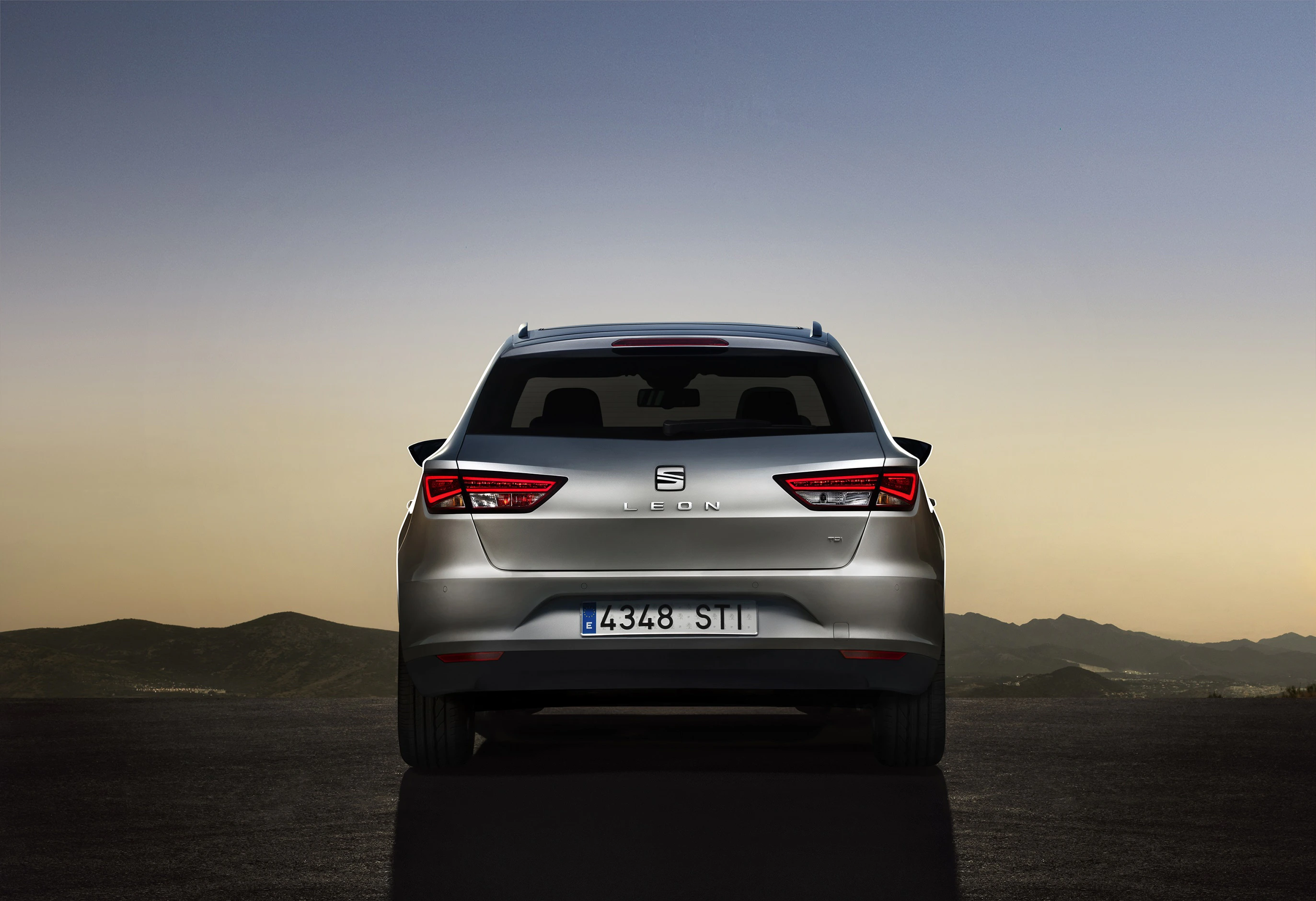 Silberner Seat Leon von hinten, bei Sonnenuntergang auf einer Straße mit Bergsilhouette im Hintergrund.