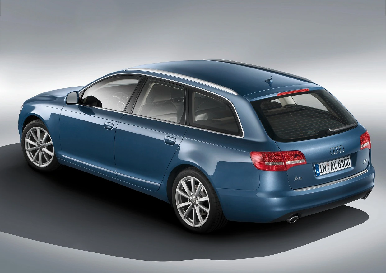 Blauer Audi A6 Avant Kombi, Ansicht von hinten links, auf grauem Hintergrund, mit silbernen Felgen und Rückleuchten in der Dämmerung.
